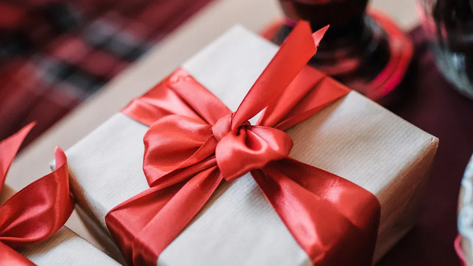 Ein schlichtes weißes Paket mit roter Schleife liegt auf einem Tisch.