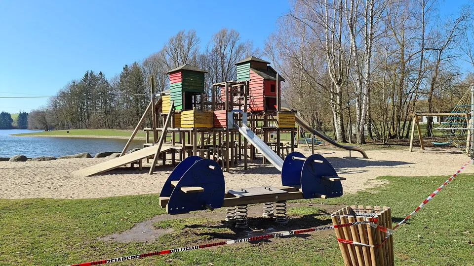 Spielplatz mit Holztürmen und Rutsche an einem See