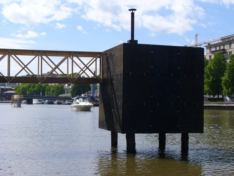 Würfelförmige schwarze Sauna mit Ofenrohr auf Pfählen über dem Wasser