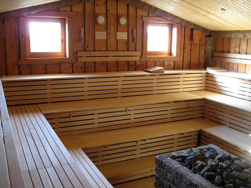 Saunakabine aus hellem Holz mit Bänken und Ofen samt Saunasteinen