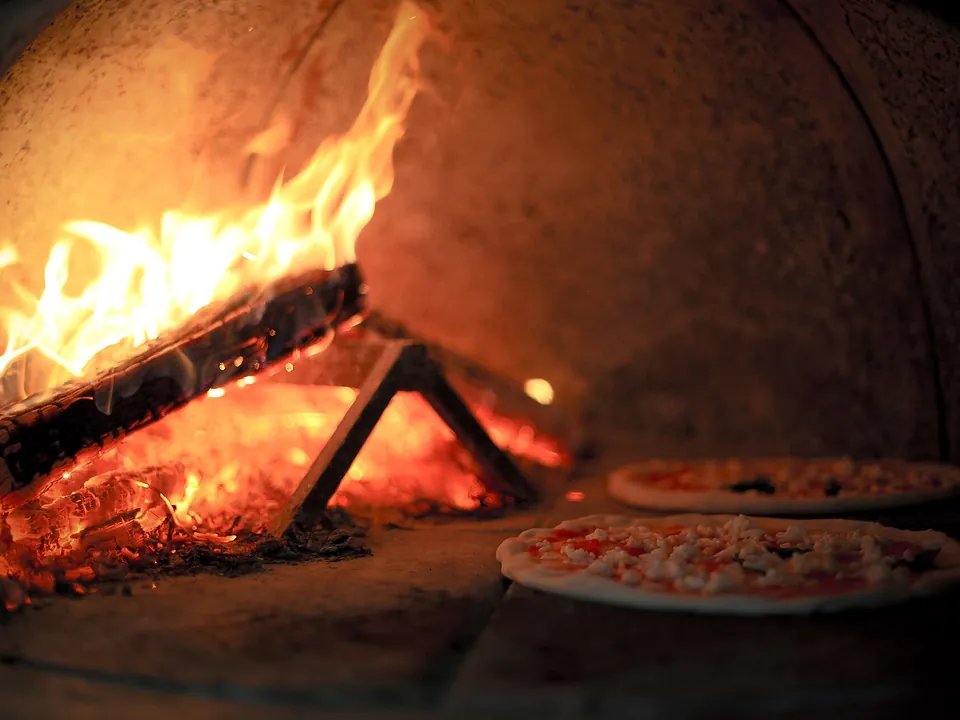 Holzfeuer in einem Steinofen, daneben backen zwei Pizzen