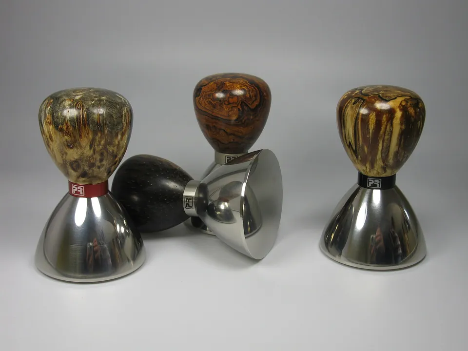 Drei Espresso-Tamper mit Holzgriffen auf grauem Grund