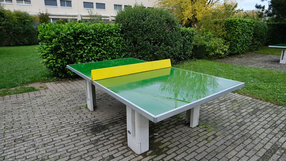 Grüne Outdoor-Tischtennisplatte mit gelbem Netz auf einem gepflasterten Platz